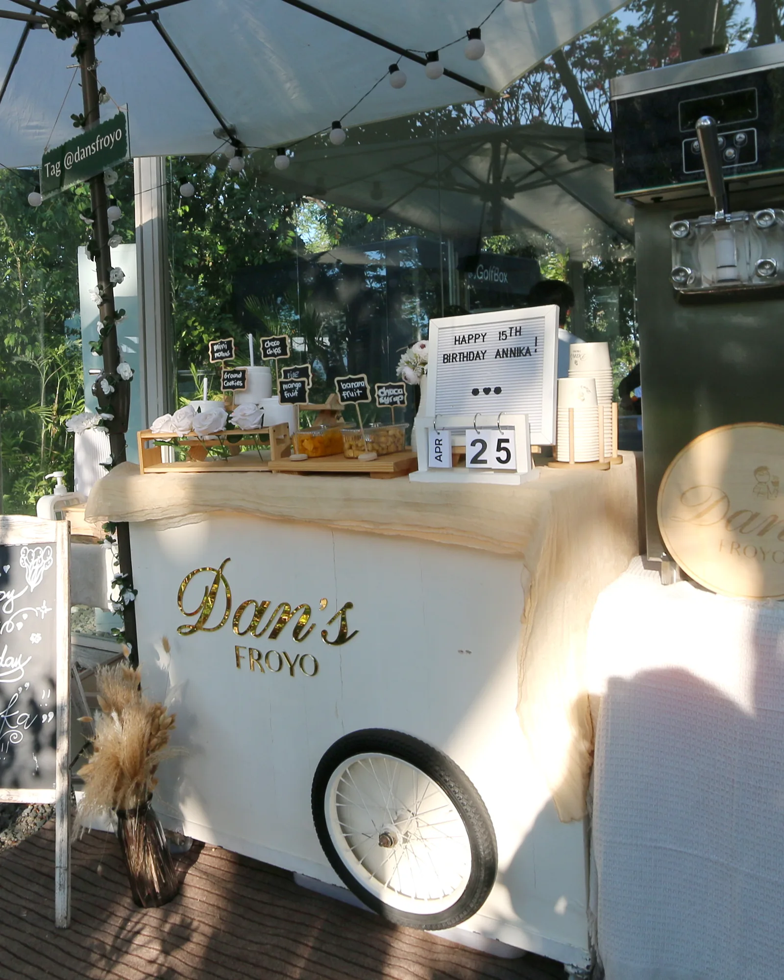 The Elegant cart in ivory and gold, styled under a white umbrella with string lights at a garden reception
